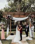 bride and groom kissing in front of a pergola draped with a white cloth