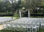 rows of chairs set up on a lawn facing a pergola draped with a white cloth 